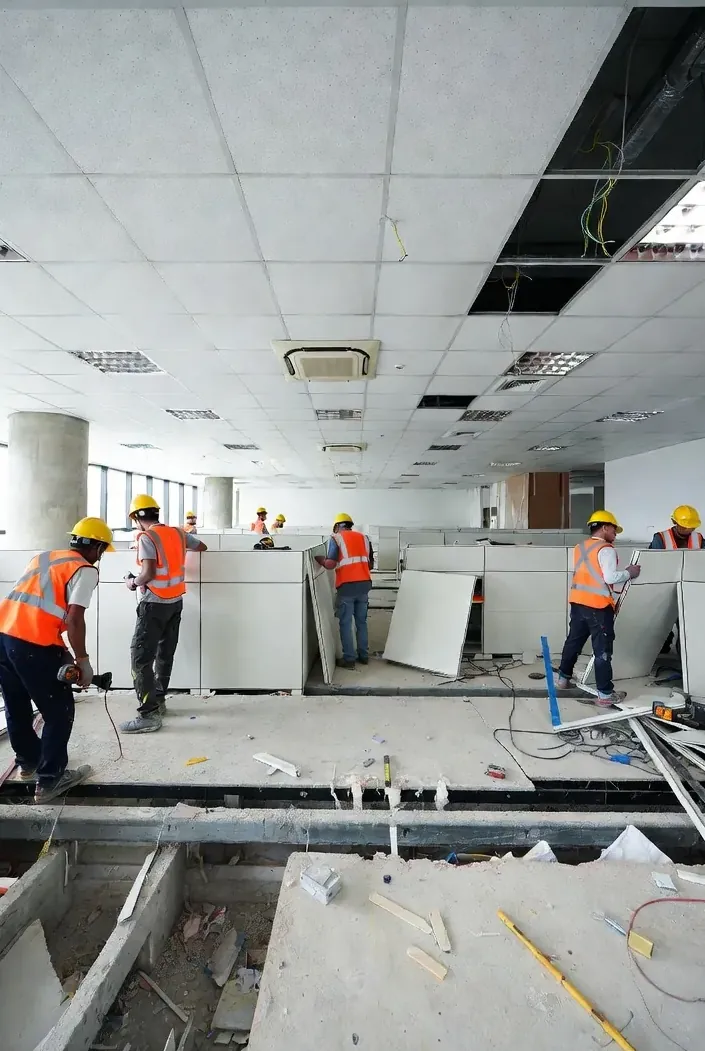 In-house reinstatement team in safety vests dismantling ceiling and partitions in an office